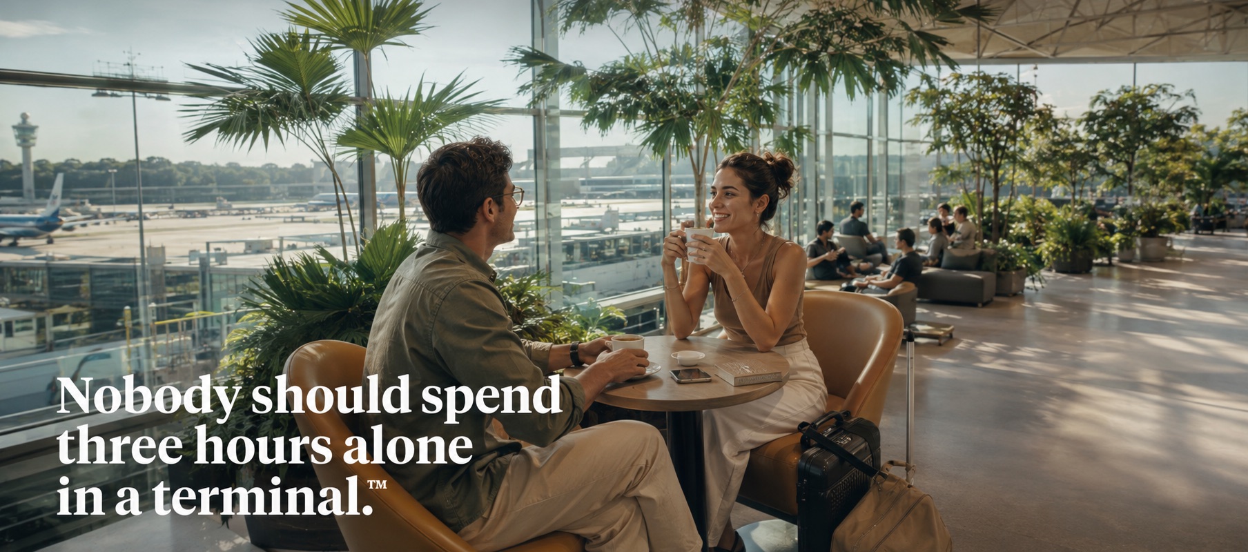 Two travellers talking over coffee at a table in a bright airport terminal, aircraft on the apron behind them. Set into the image: Nobody should spend three hours alone in a terminal.
